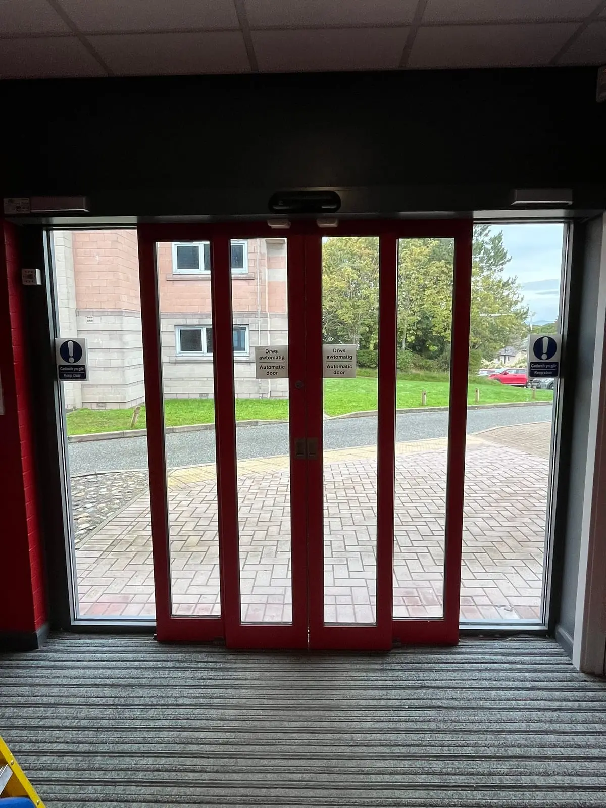 Red-framed automatic sliding double doors with bilingual automatic door signs