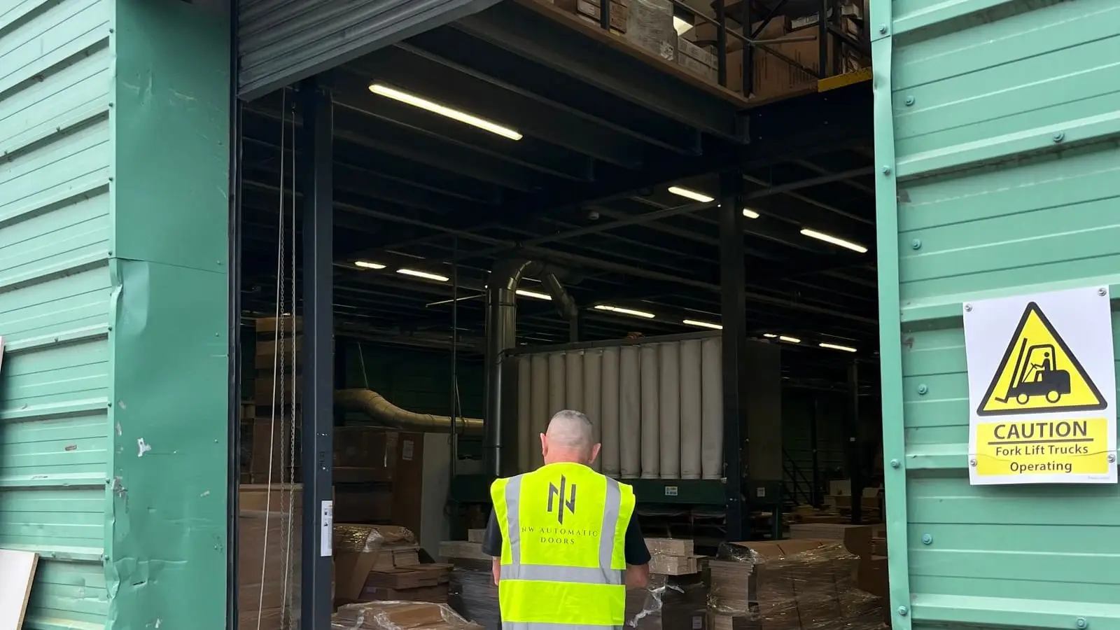 Engineer in hi-vis, seen from behind, walking through an open roller shutter into a warehouse