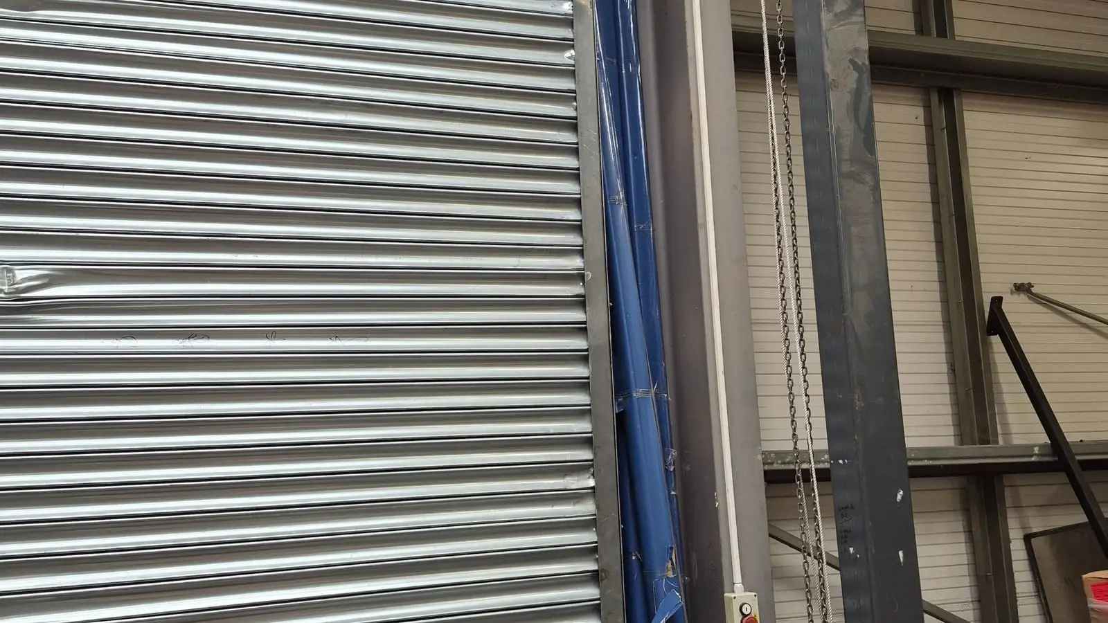 Large silver roller shutter with impact dents inside an industrial unit