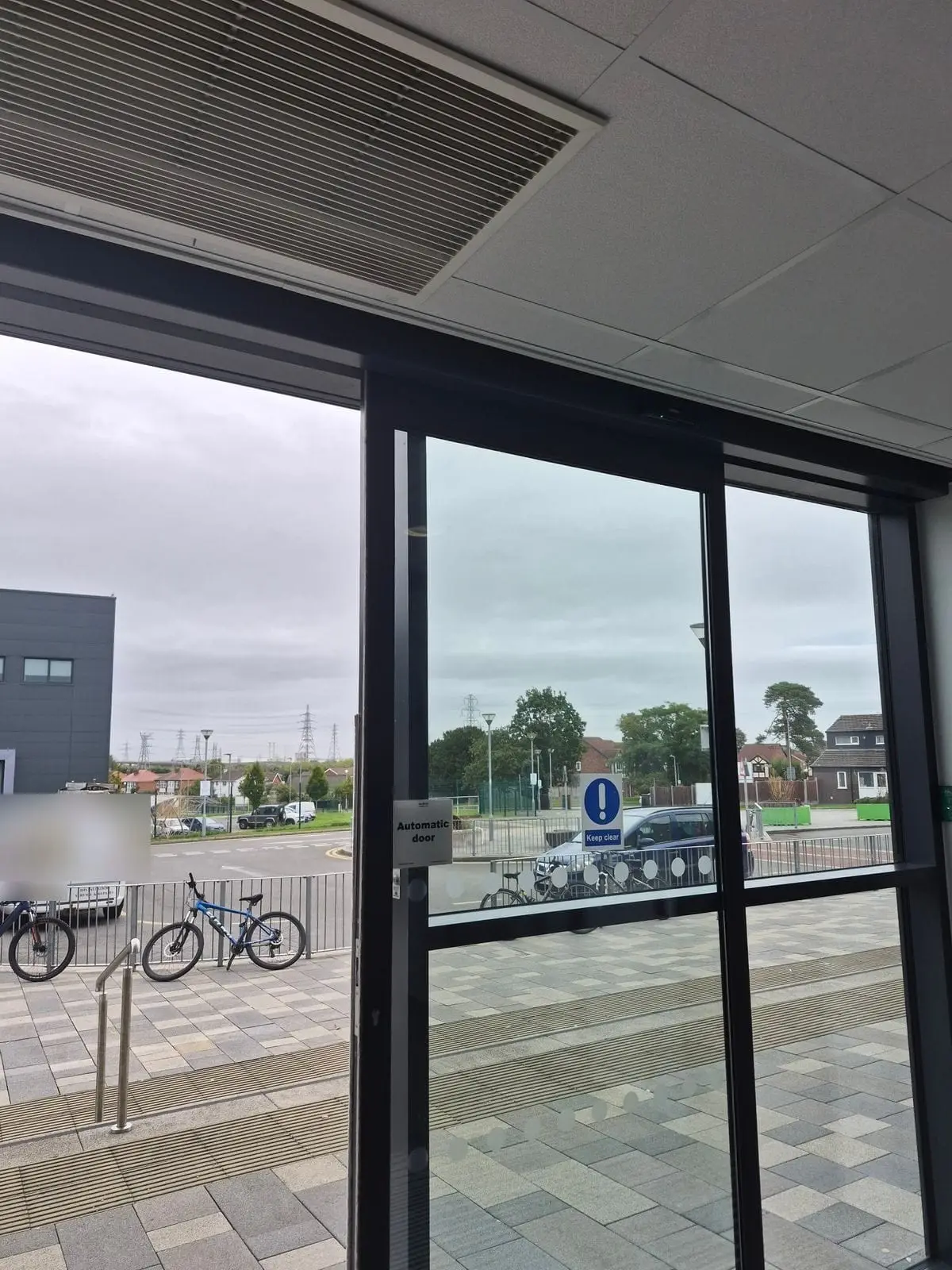 Automatic sliding door with automatic door and keep clear signs, seen from inside and looking out to a car park