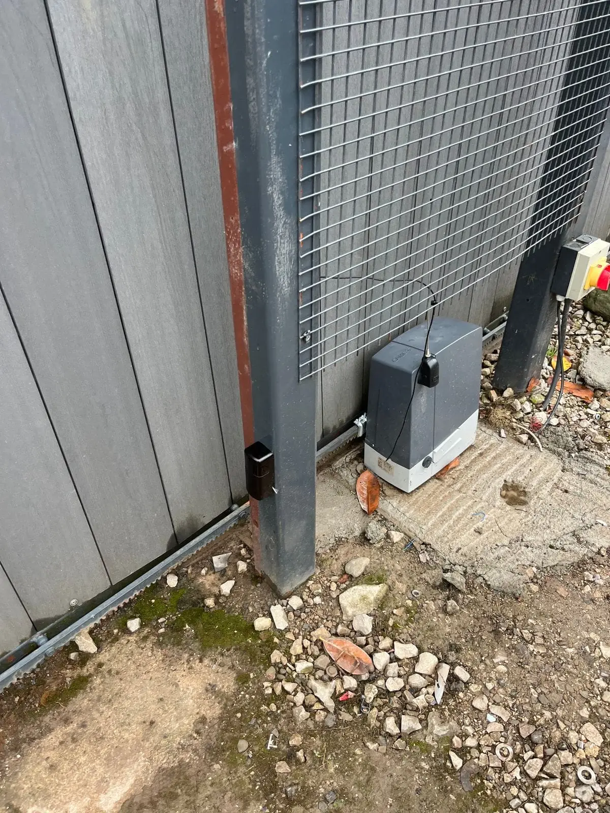 Sliding gate operator and rack beside a timber-clad boundary
