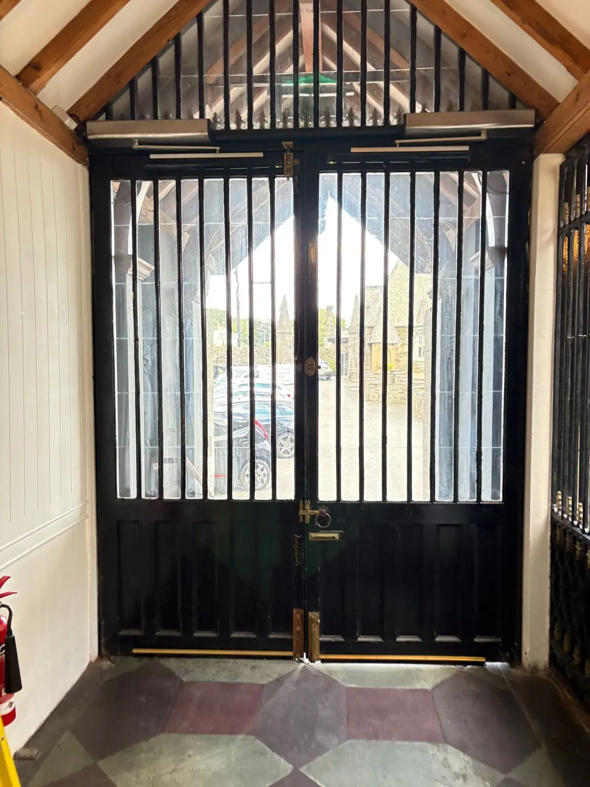 Black wrought-iron double doors with automatic operators in a timber-framed porch